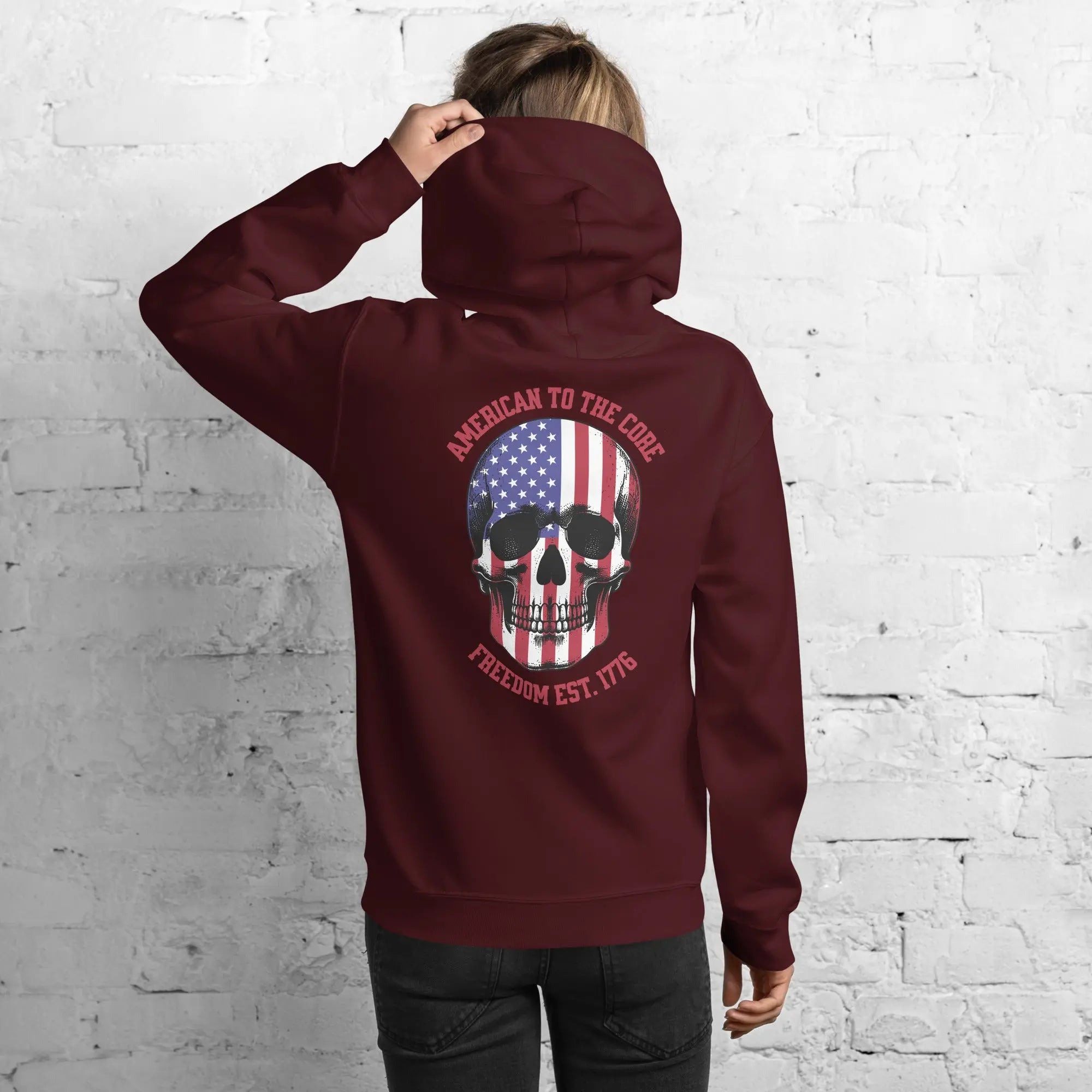 Back of a woman wearing a maroon patriotic hoodie with a skull and the text "American to the core. Freedom Est. 1776." 