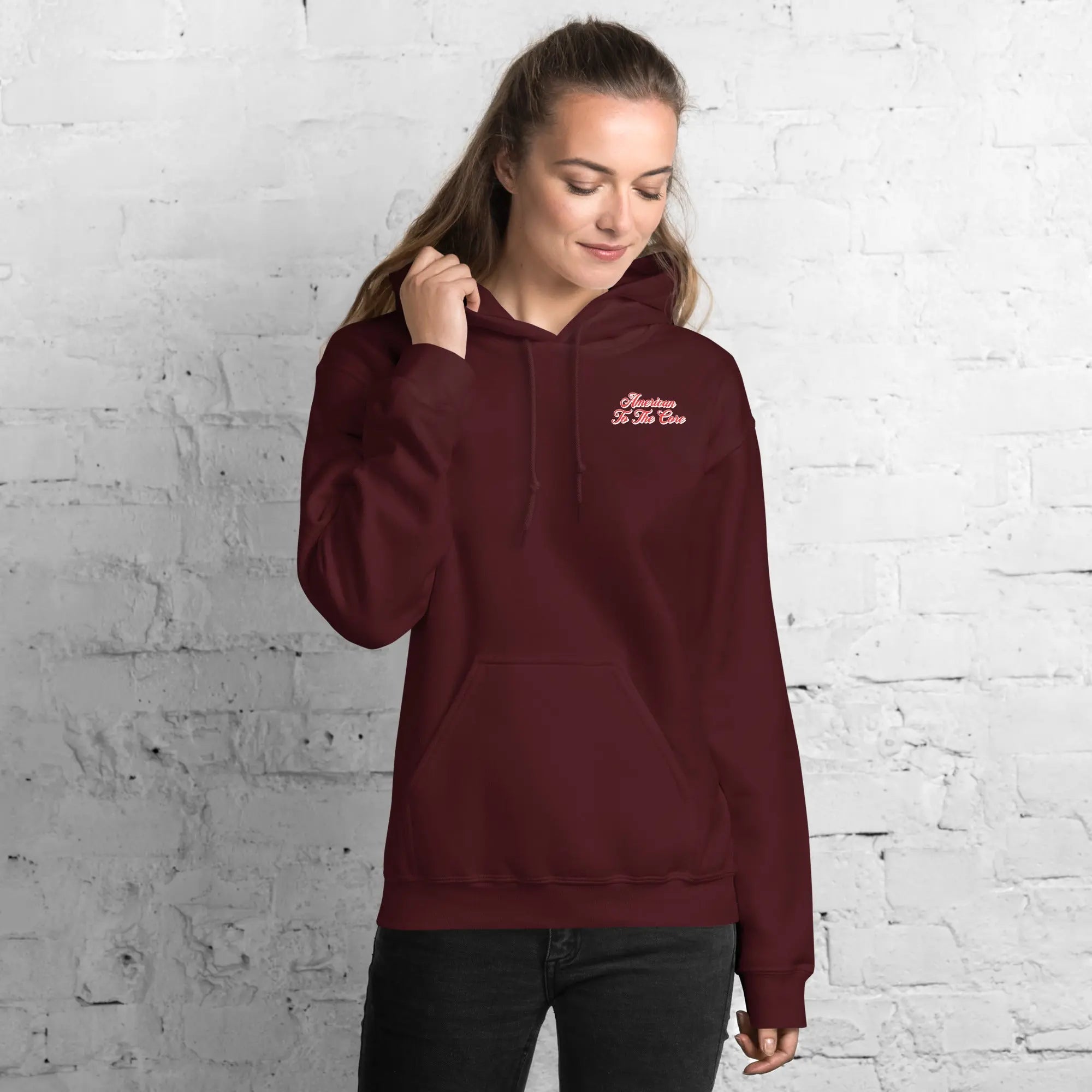 A woman wearing a maroon, patriotic hoodie with the text "American to the core."