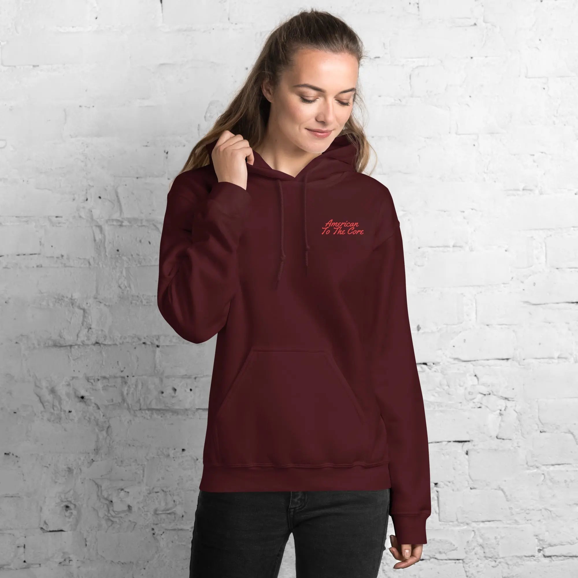 A woman wearing a maroon patriotic hoodie with the text "American To The Core."