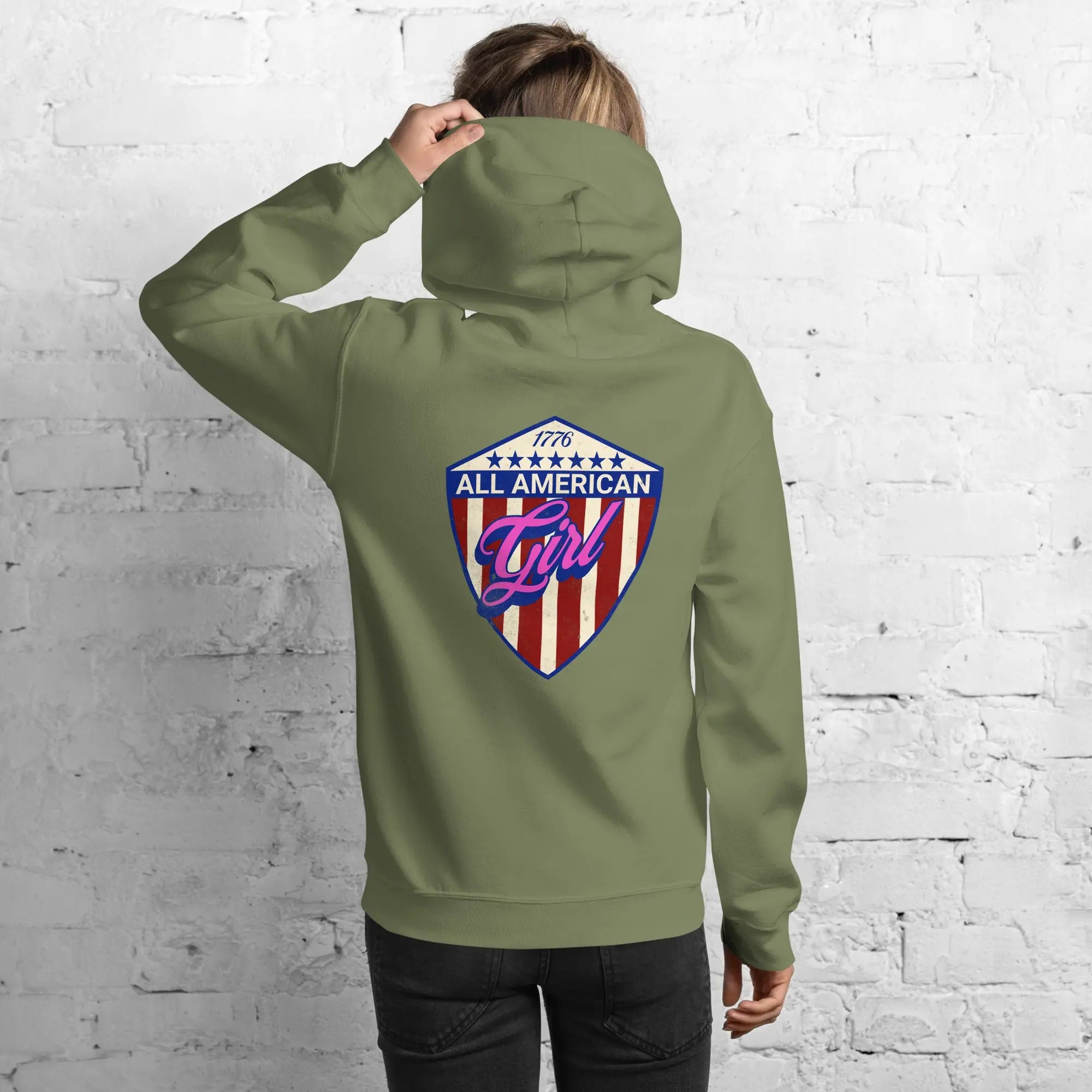 Back of a woman wearing a patriotic military green hoodie with the text "All American Girl" over a patriotic design. 