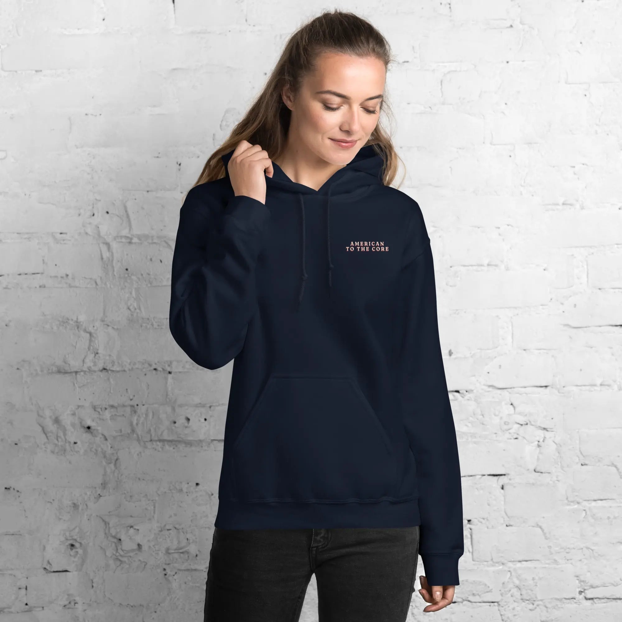 A woman wearing a navy patriotic hoodie with the text "American to the core."