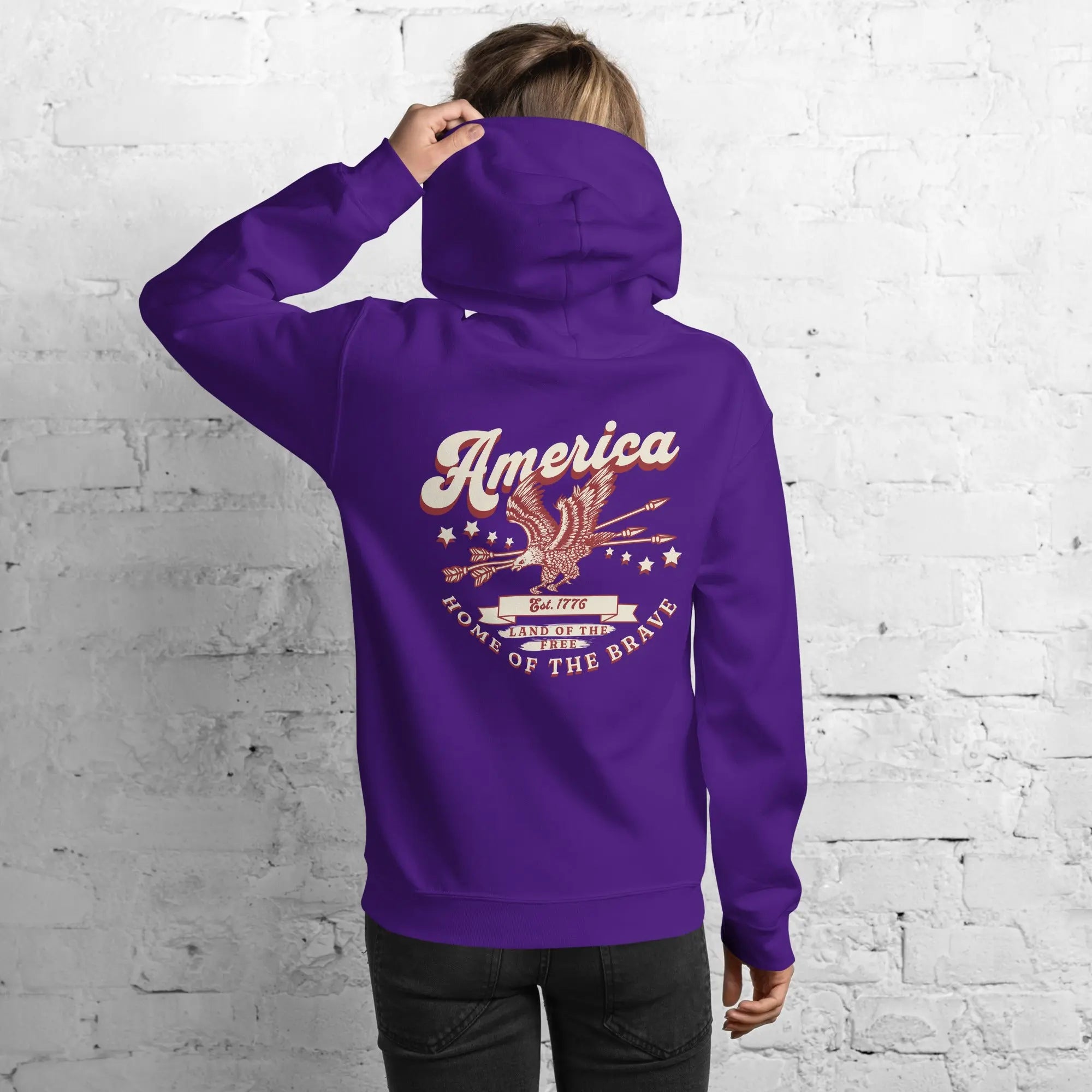 Back of a woman wearing a purple patriotic hoodie with an eagle and the text "America home of the brave."