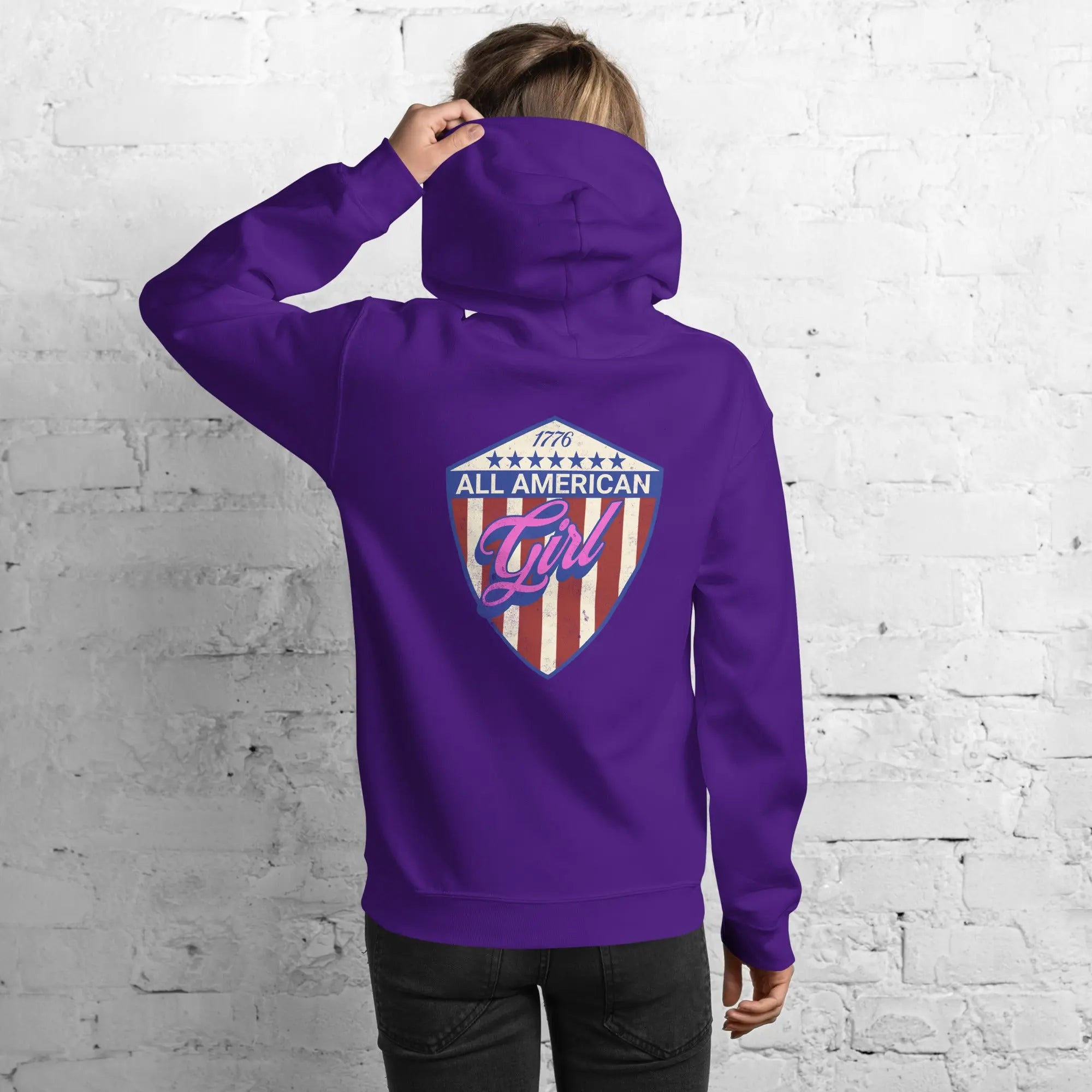 Back of a woman wearing a patriotic purple hoodie with the text "All American Girl" over a patriotic design. 