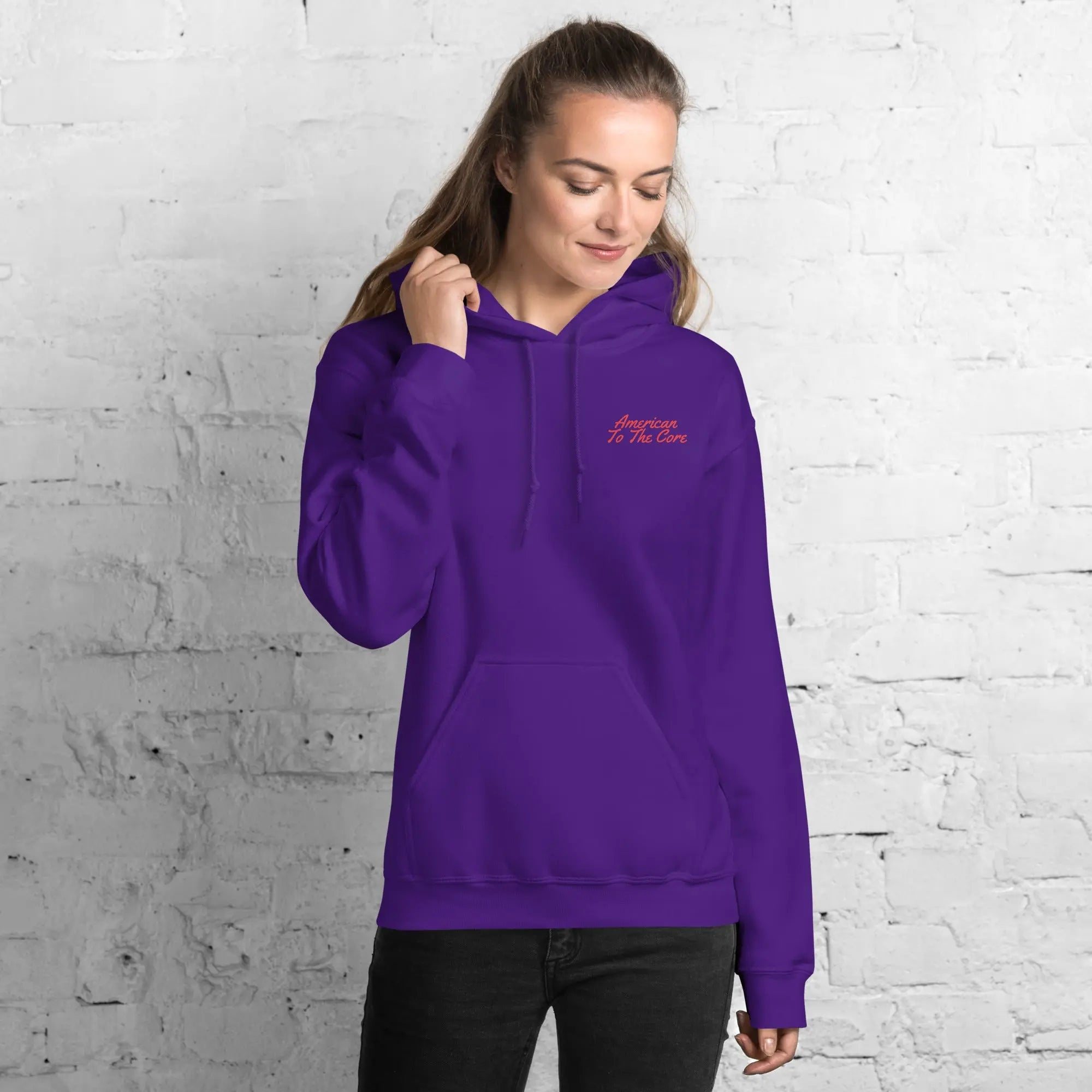 A woman wearing a purple patriotic hoodie with the text "American To The Core." 