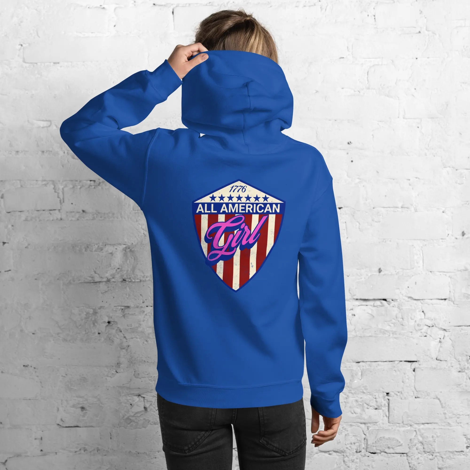 Back of a woman wearing a patriotic royal blue hoodie with the text "All American Girl" over a patriotic design. 