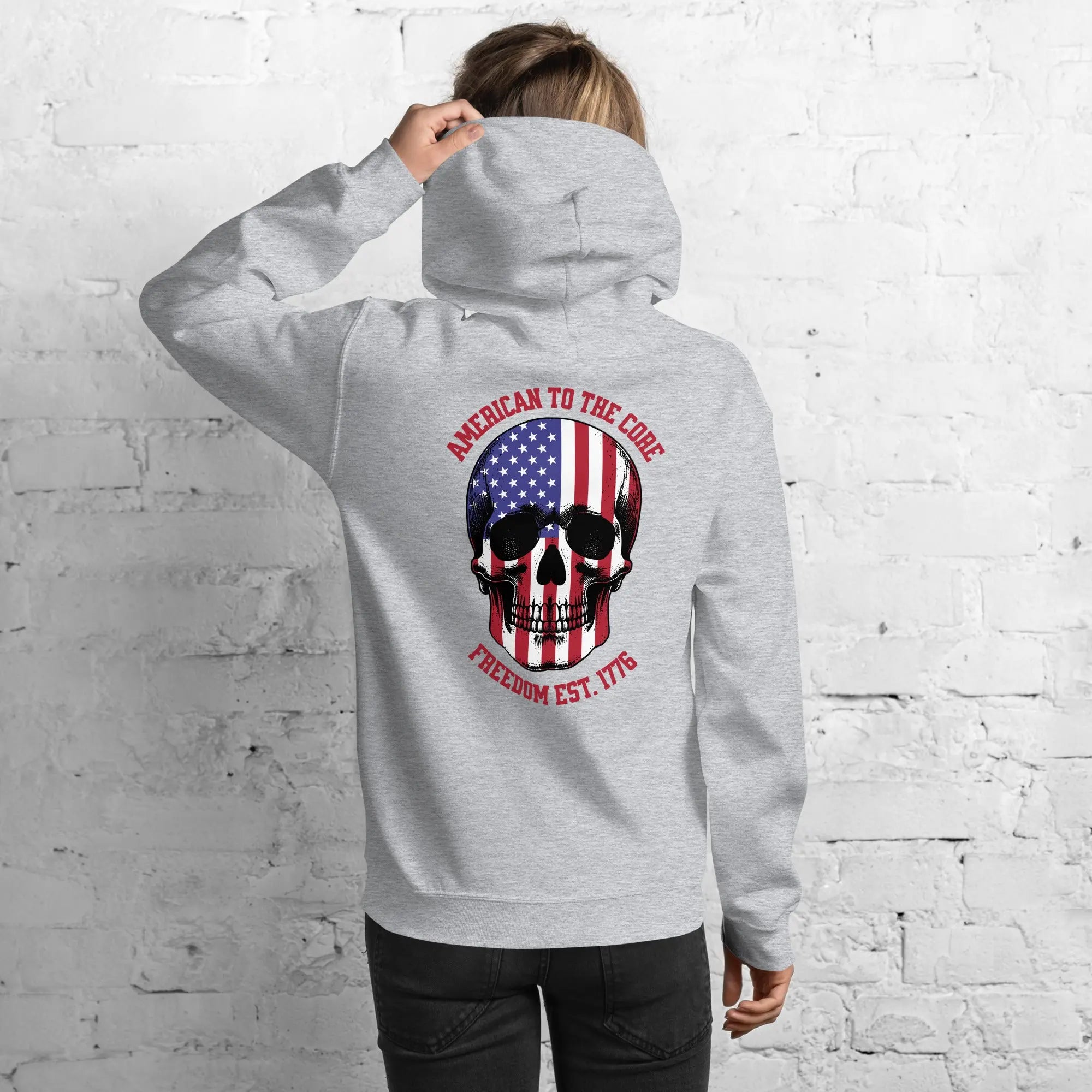 Back of a woman wearing a sport grey patriotic hoodie with a skull and the text "American to the core. Freedom Est. 1776." 
