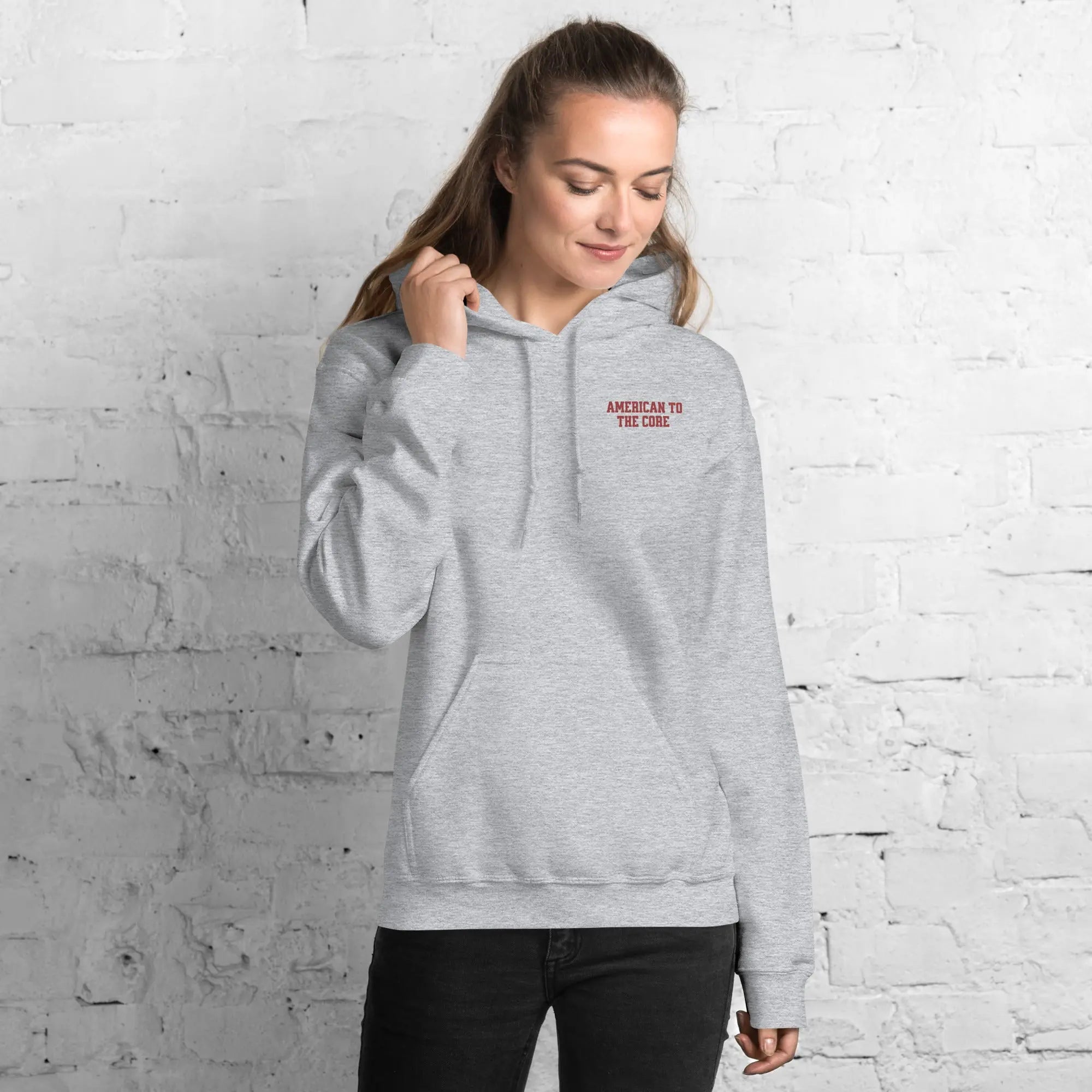 A woman wearing a sport grey patriotic hoodie with "American to the core." 
