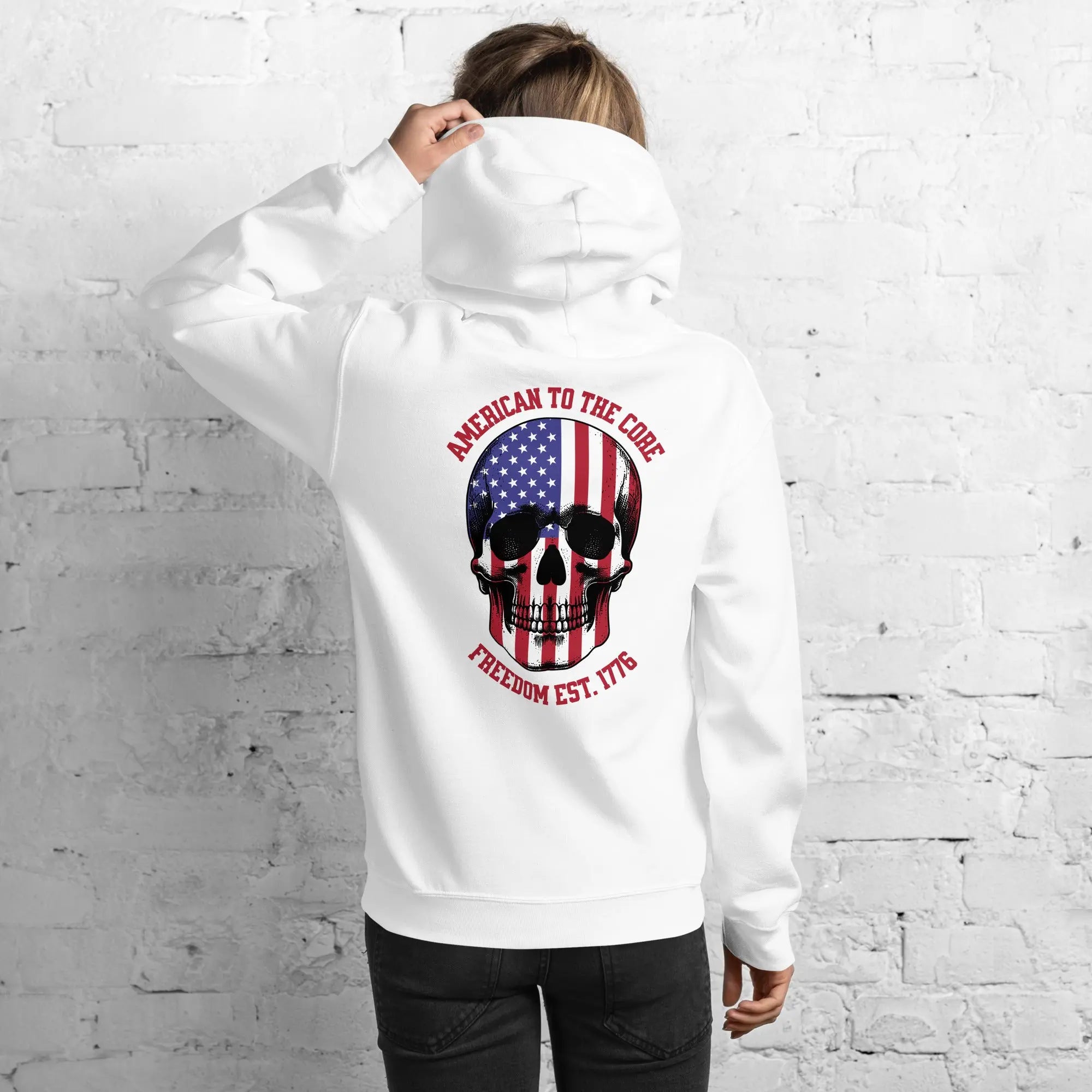 Back of a woman wearing a white patriotic hoodie with a skull and the text "American to the core. Freedom est. 1776." 