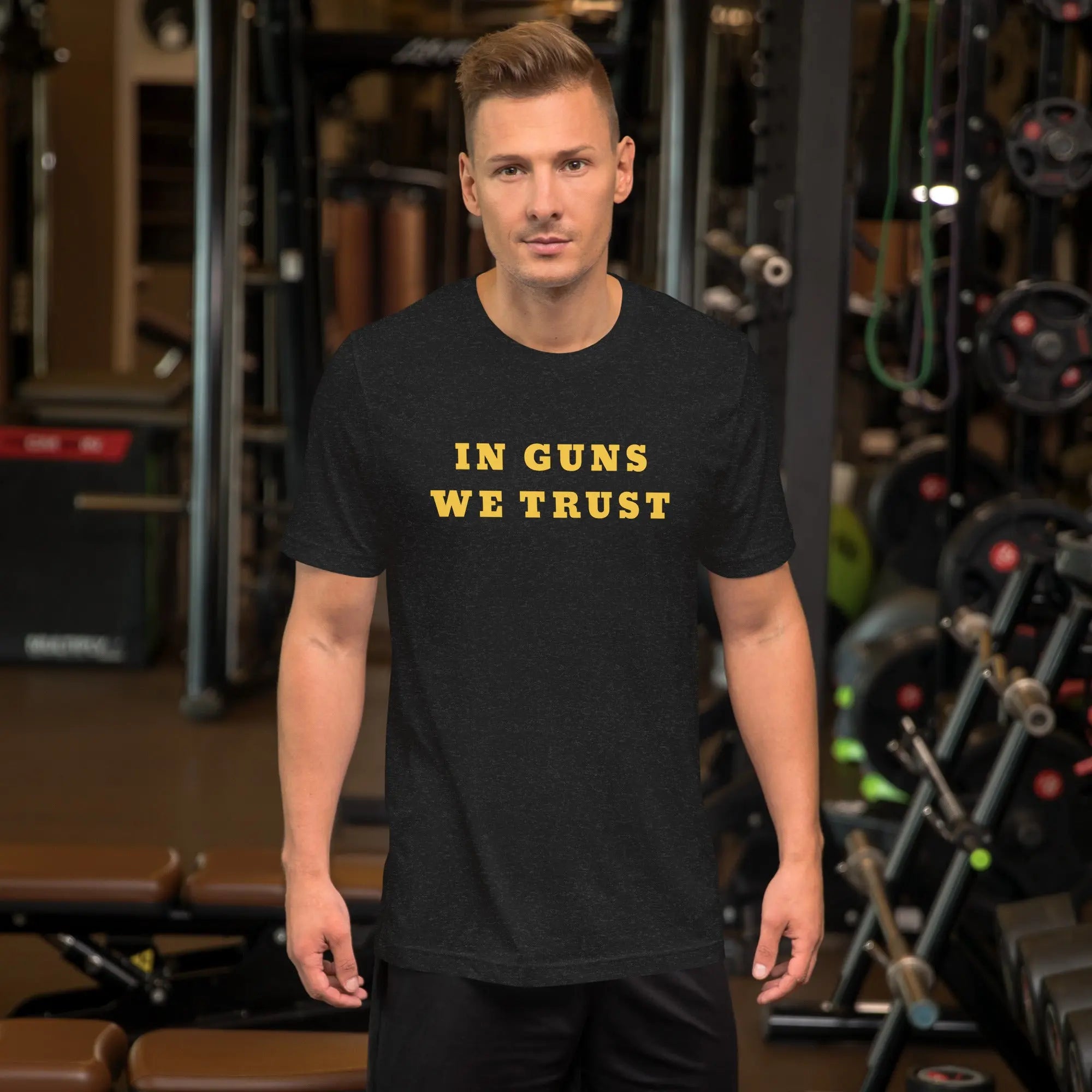 A man wearing a black heather patriotic t-shirt with yellow "In Guns We Trust" text.
