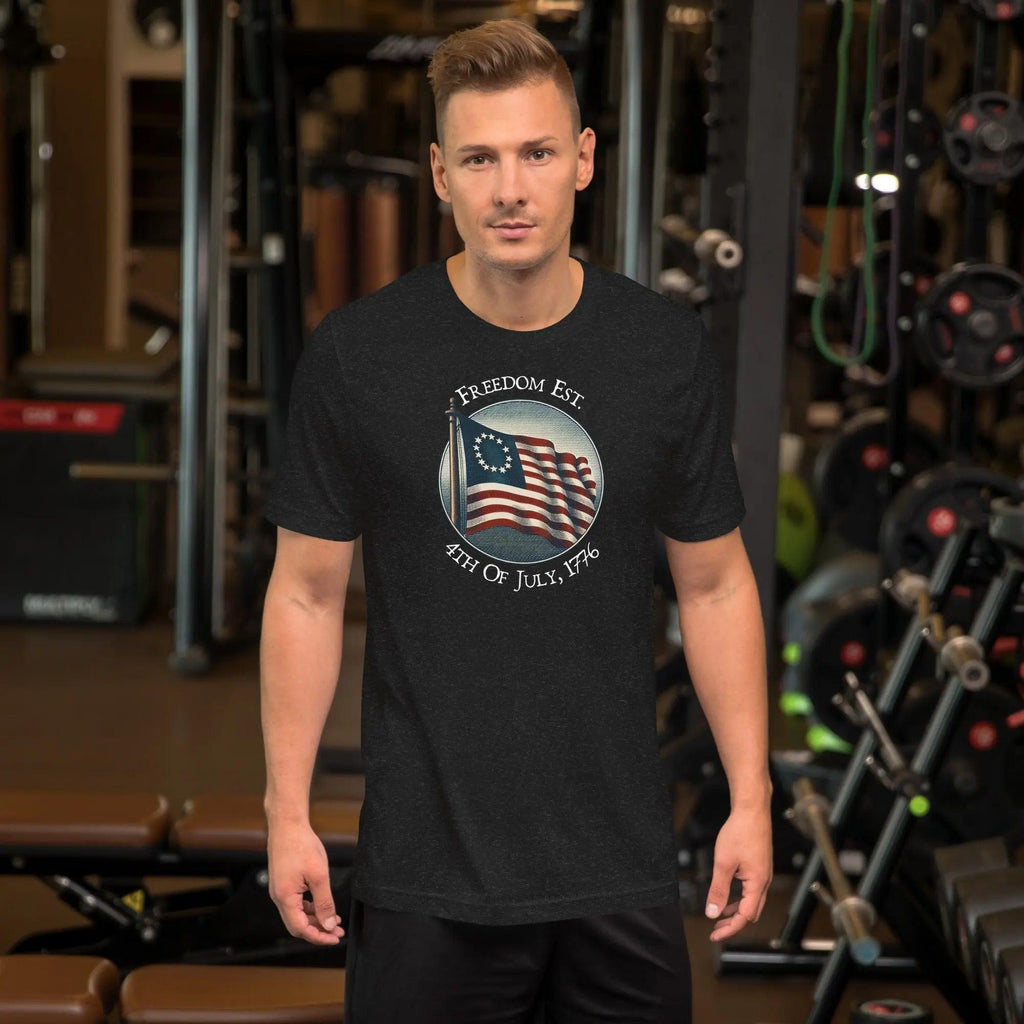 A man wearing a black heather patriotic t-shirt. With the American flag and the text "Freedom est. 4th of July, 1776." 