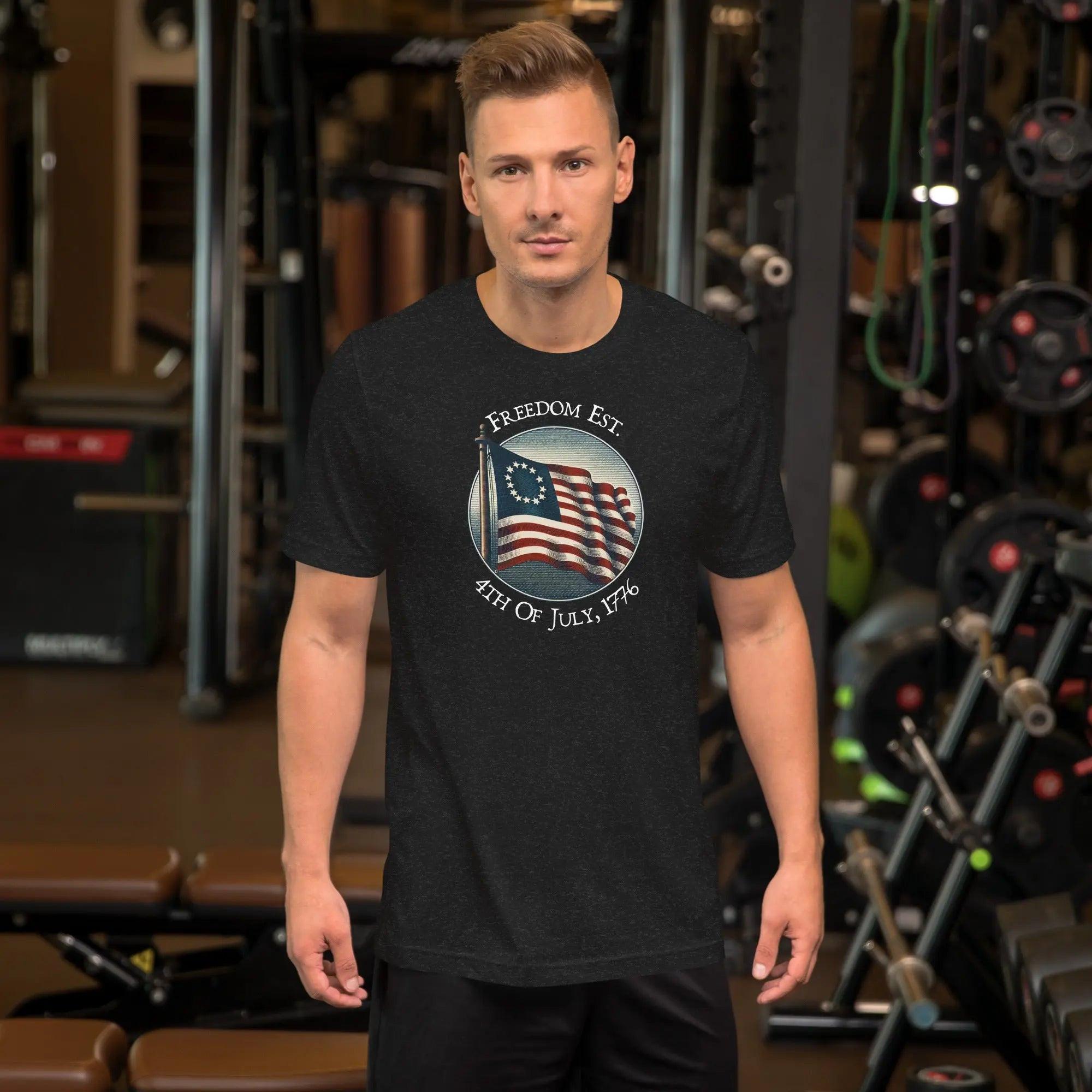 A man wearing a black heather patriotic t-shirt. With the American flag and the text "Freedom est. 4th of July, 1776." 