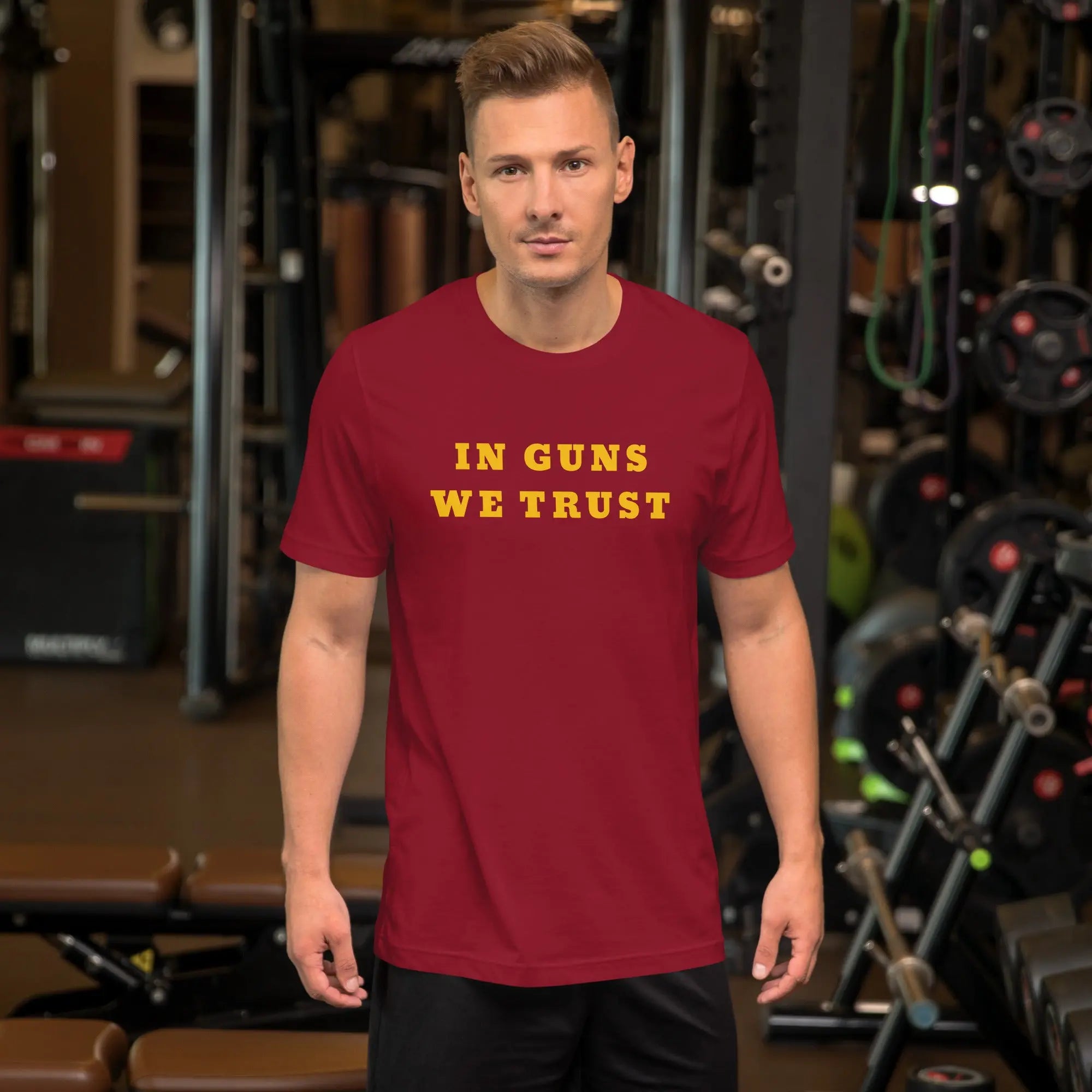 A man wearing a cardinal patriotic t-shirt with yellow "In Guns We Trust" text.