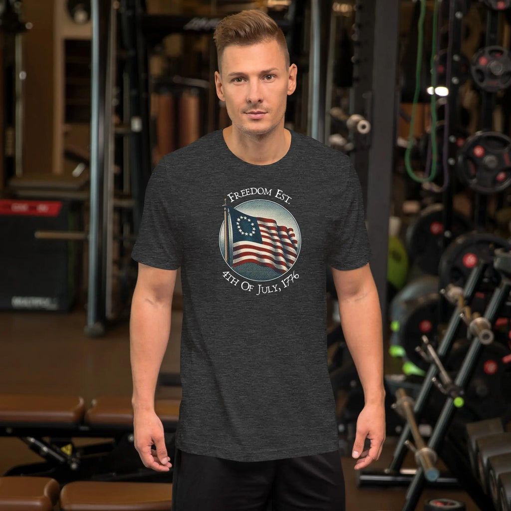 A man wearing a dark grey heather patriotic t-shirt. With the American flag and the text "Freedom est. 4th of July, 1776." 