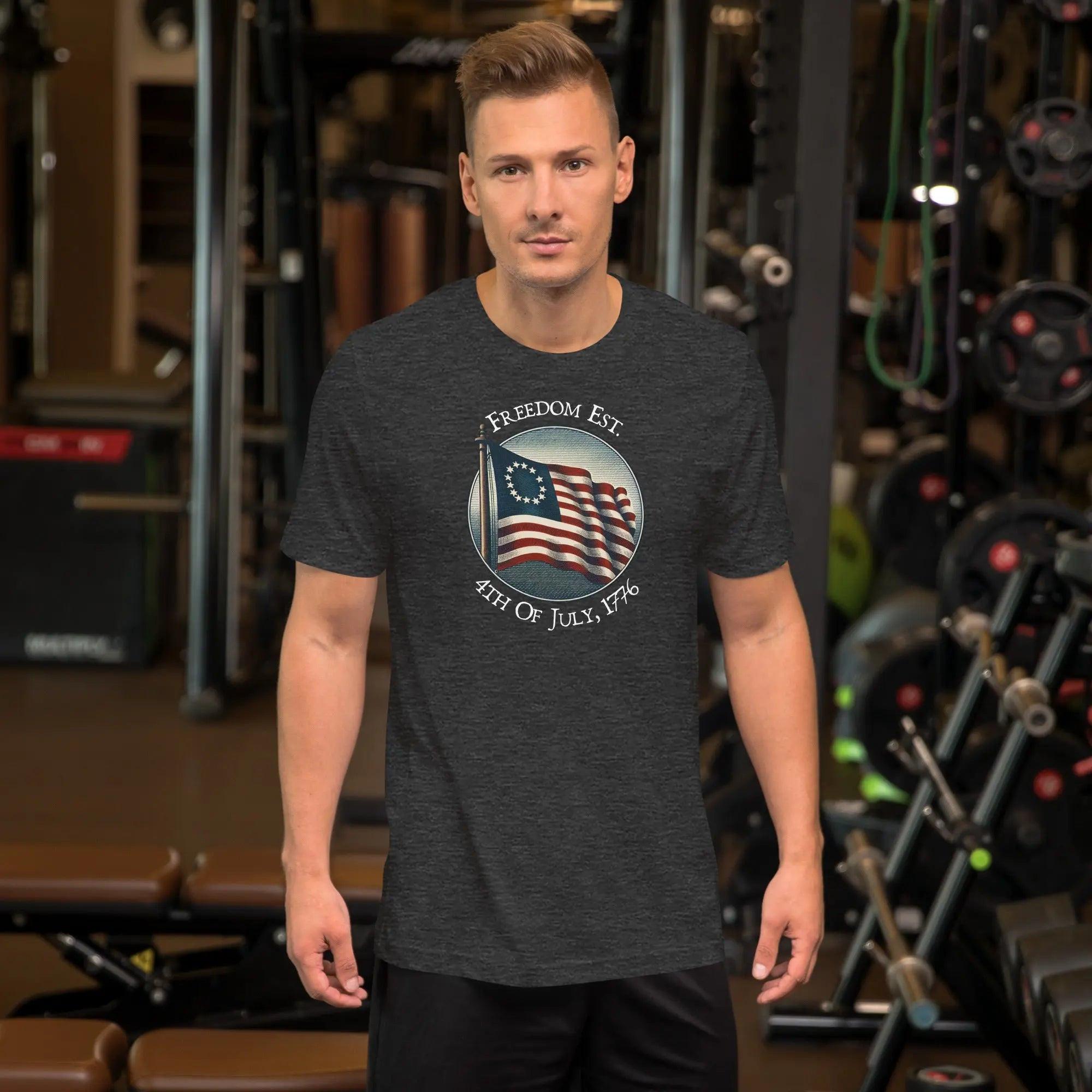 A man wearing a dark grey heather patriotic t-shirt. With the American flag and the text "Freedom est. 4th of July, 1776." 
