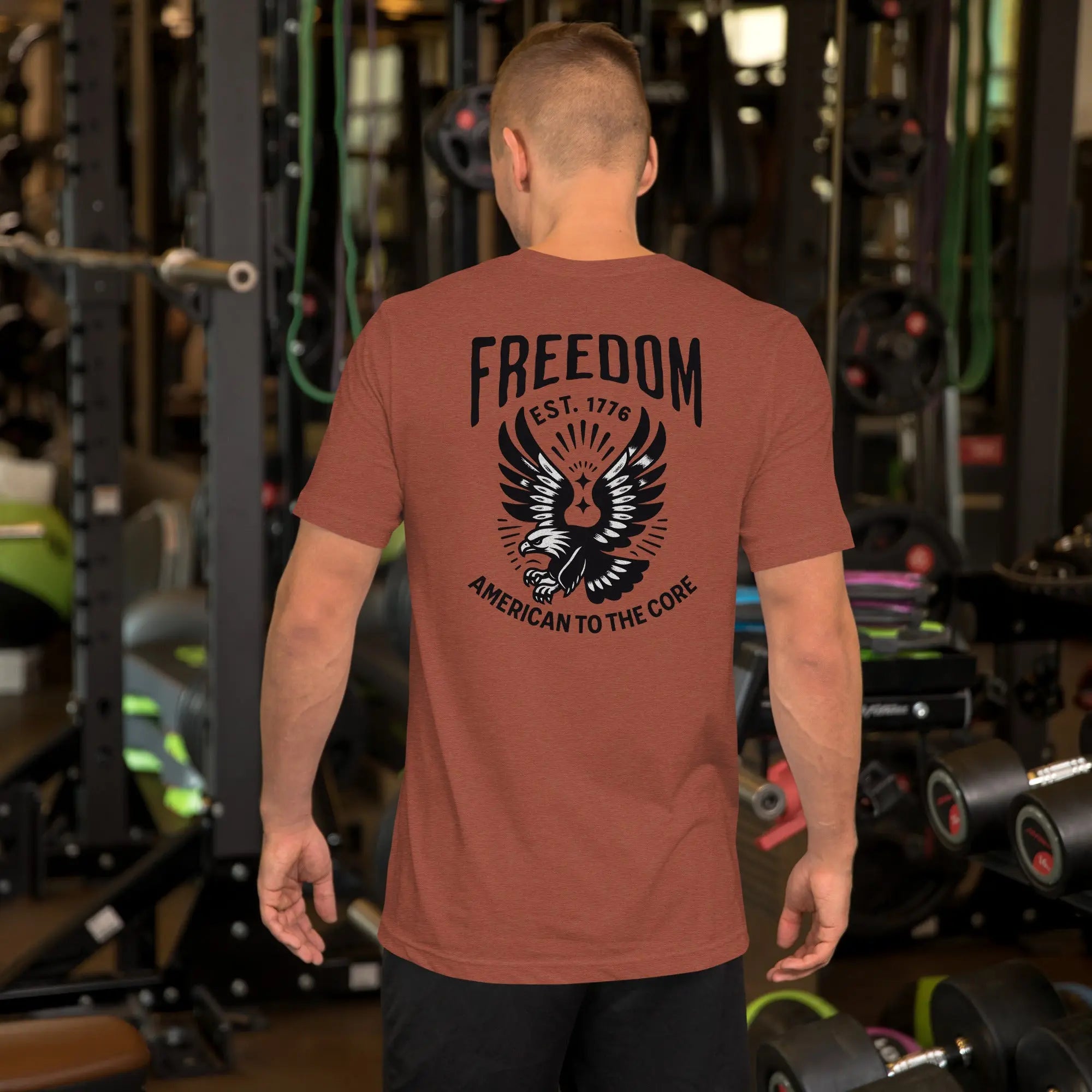 Back of man wearing a heather clay patriotic t-shirt with an eagle and "freedom est. 1776" text