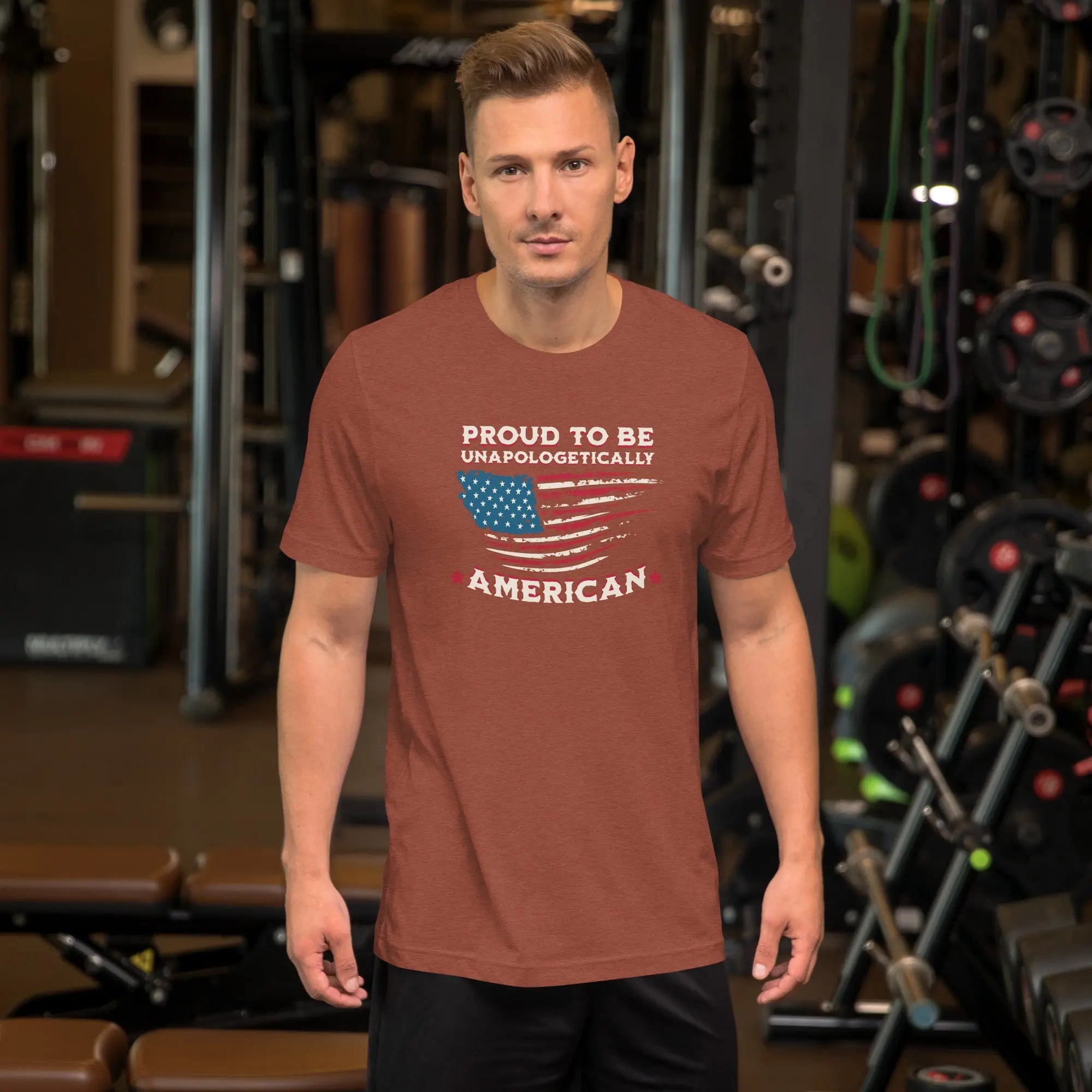 A man wearing a heather clay patriotic t-shirt with the american Flag and the text "Proud To be Unapologetically American"
