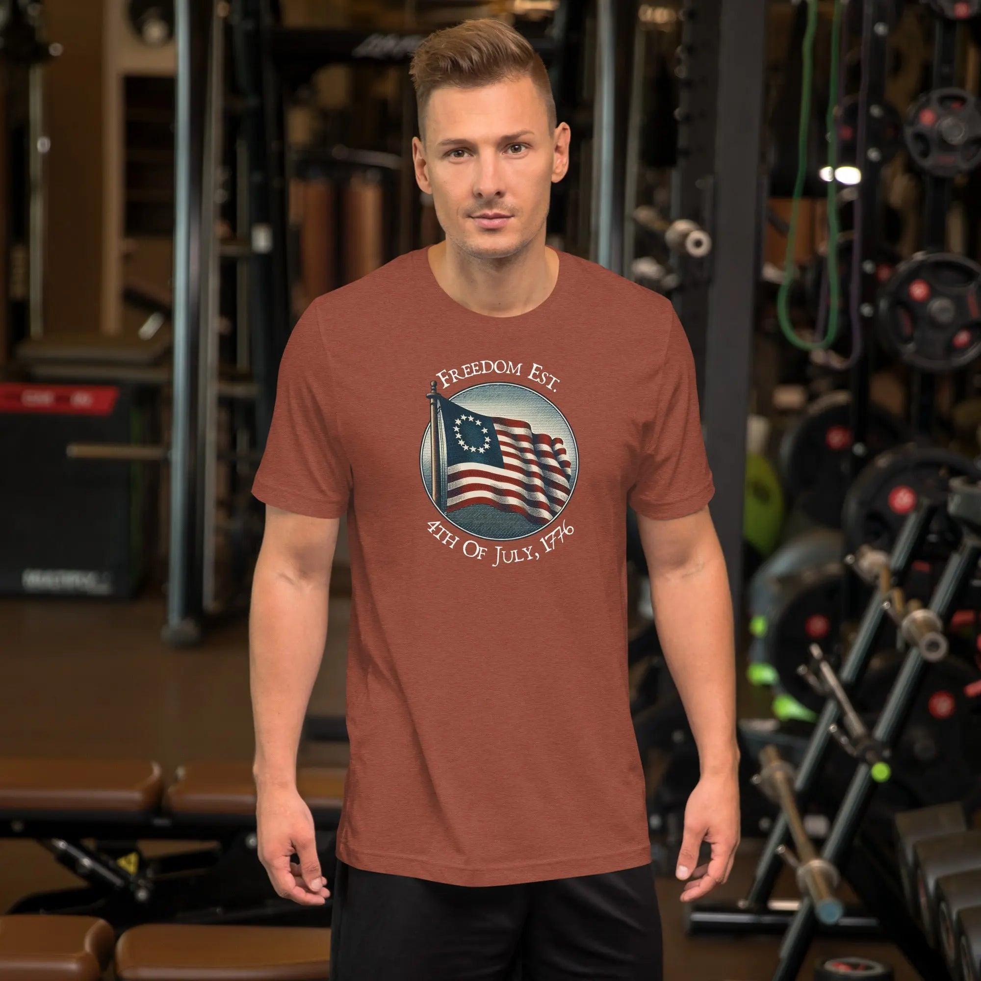 A man wearing clay heather patriotic t-shirt. With the American flag and the text "Freedom est. 4th of July, 1776." 