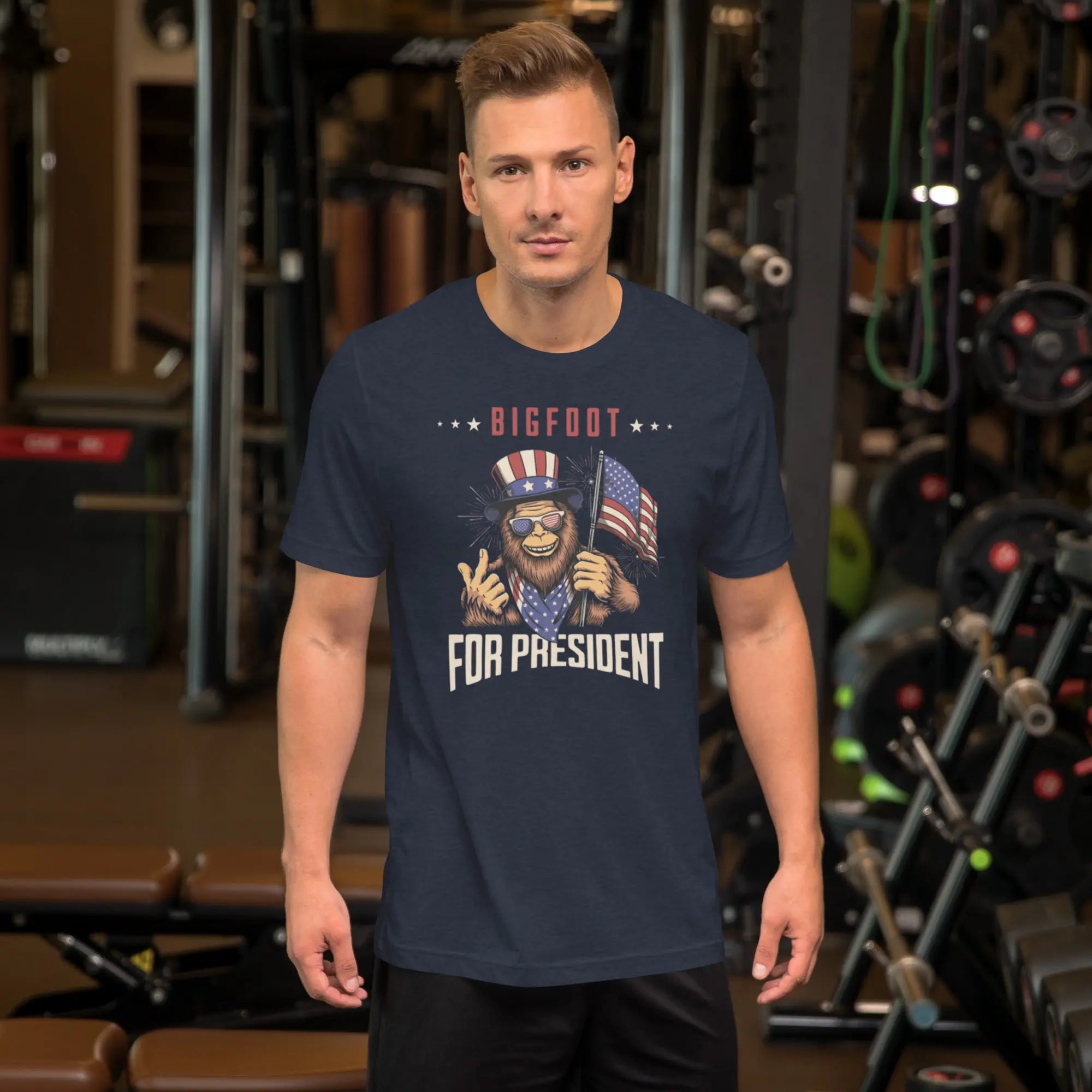 man wearing a heather navy blue patriotic t-shirt with a image of bigfoot with "Bigfoot for president" text