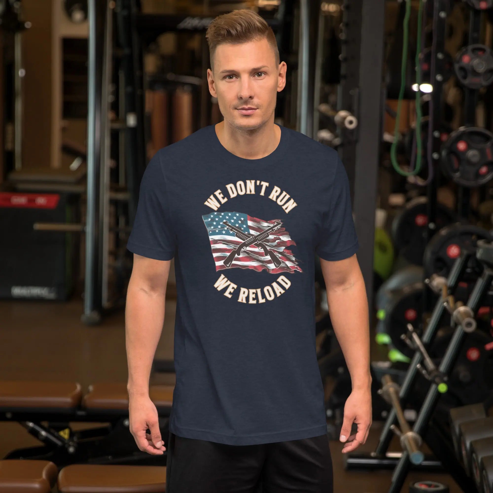 A man wearing a navy heather patriotic t-shirt with shotguns over the American flag and the "We don't run, we reload" text.
