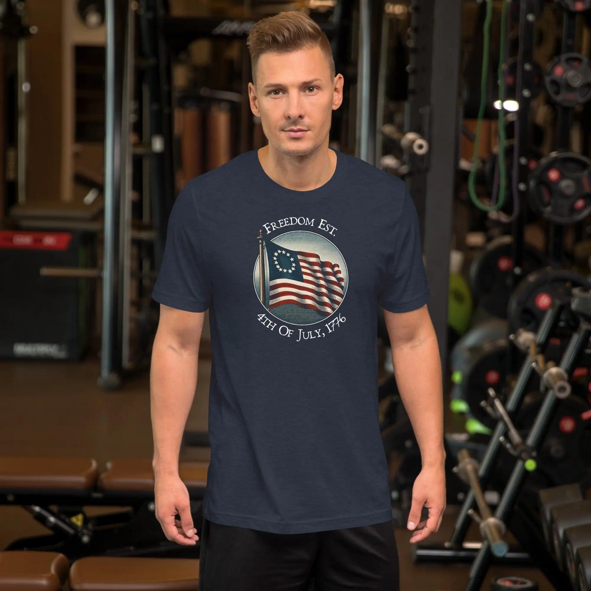 A man wearing a heather navy patriotic t-shirt. With the American flag and the text "Freedom est. 4th of July, 1776." 