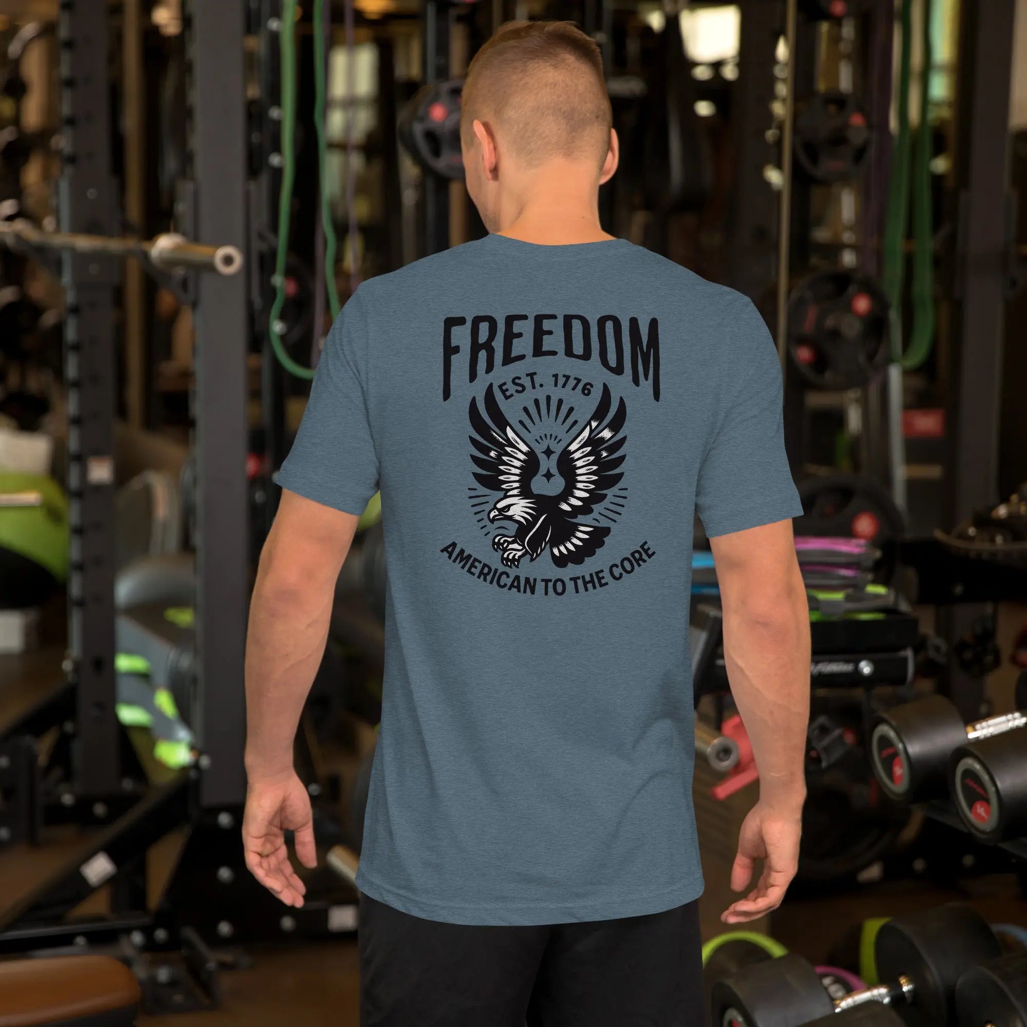 Back of man wearing a heather slate patriotic t-shirt with an eagle and "freedom est. 1776" text
