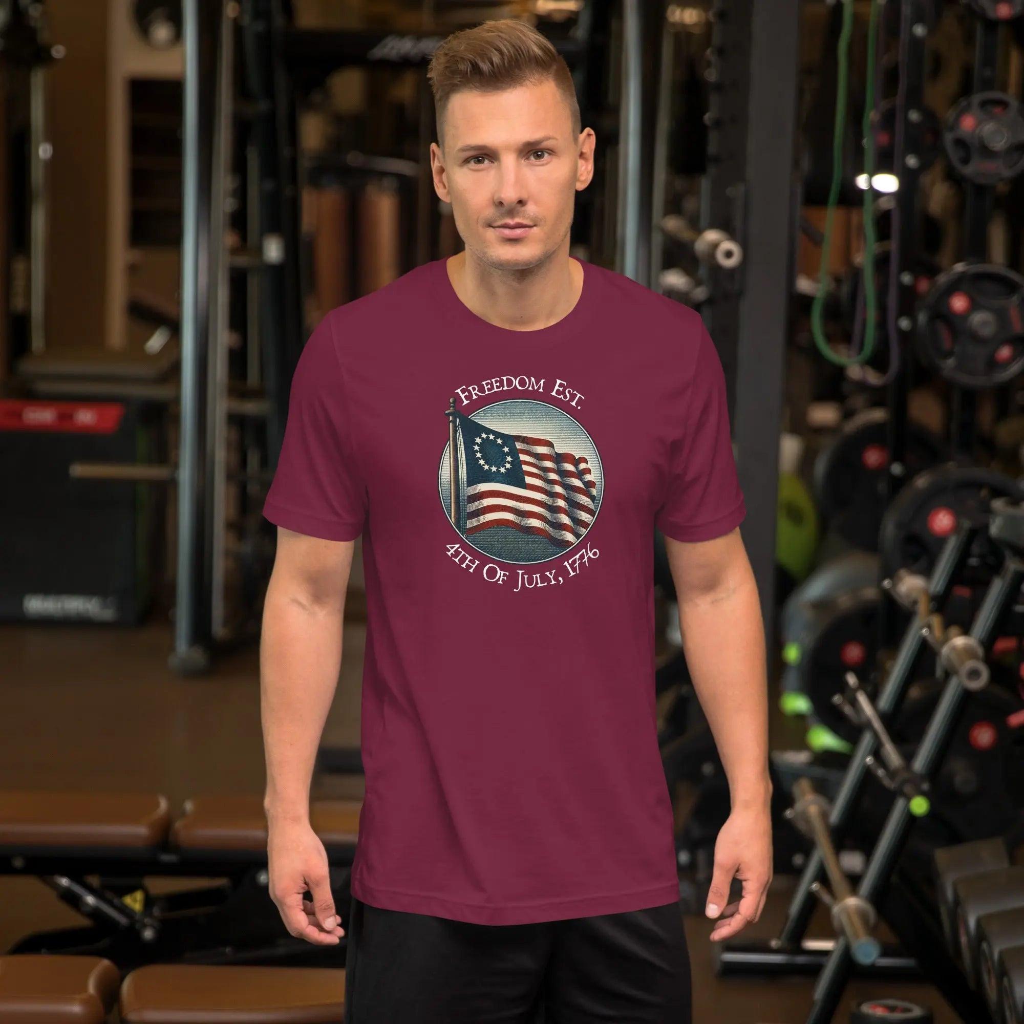 A man wearing a maroon patriotic t-shirt. With the American flag and the text "Freedom est. 4th of July, 1776." 