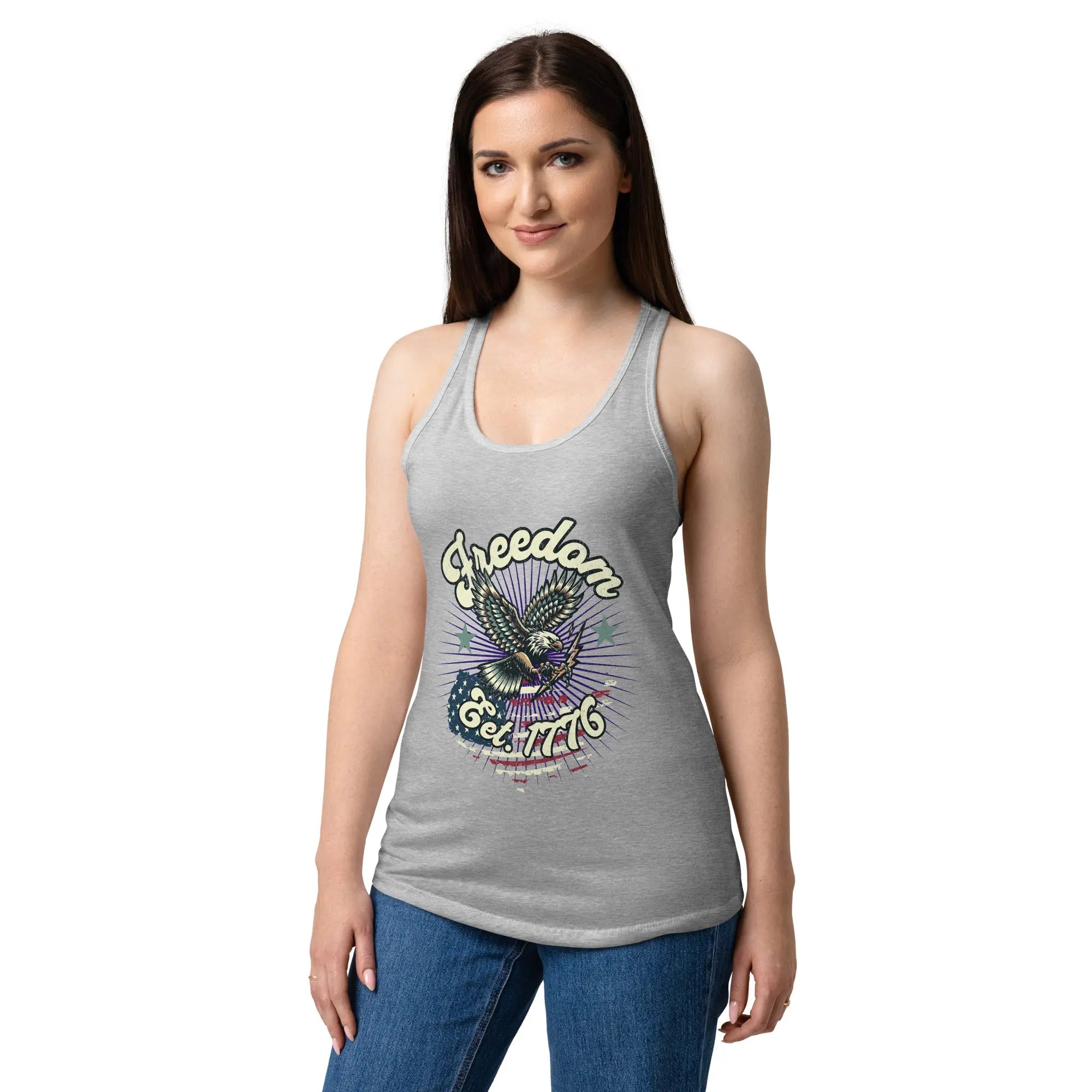 A woman wearing a heather grey, fitted, patriotic racerback tank top with a flying eagle and the text "Freedom est. 1776."