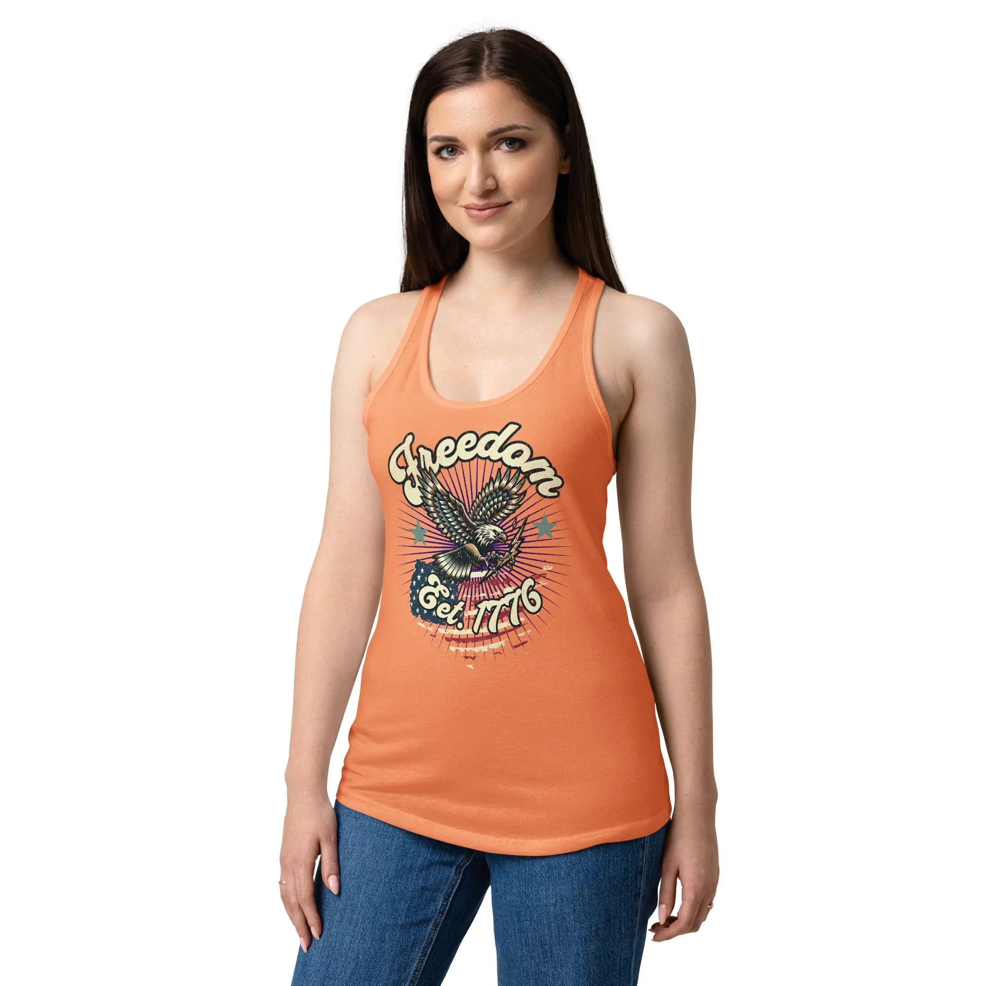 A woman wearing a light orange, fitted, patriotic racerback tank top with a flying eagle and the text "Freedom est. 1776."