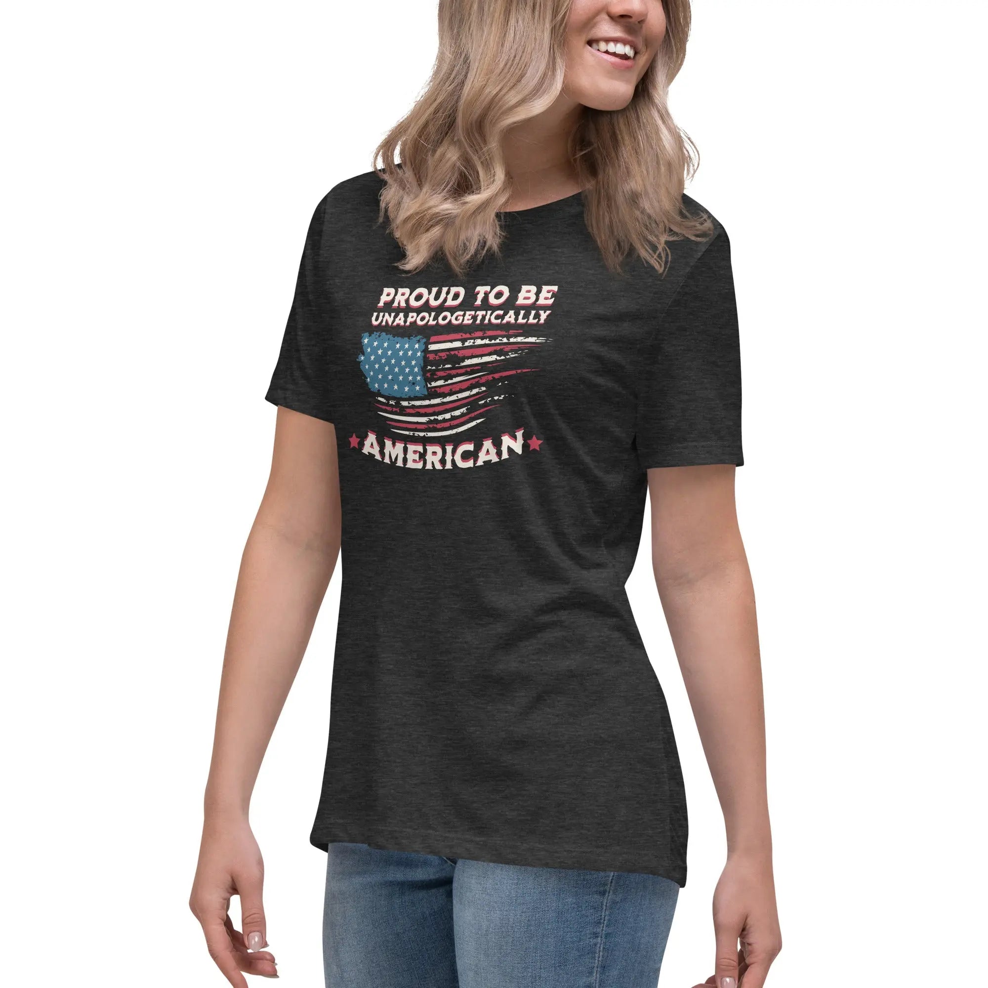 A woman wearing a dark grey heather patriotic t-shirt with the American flag and "Proud To Be Unapologetically American" text.