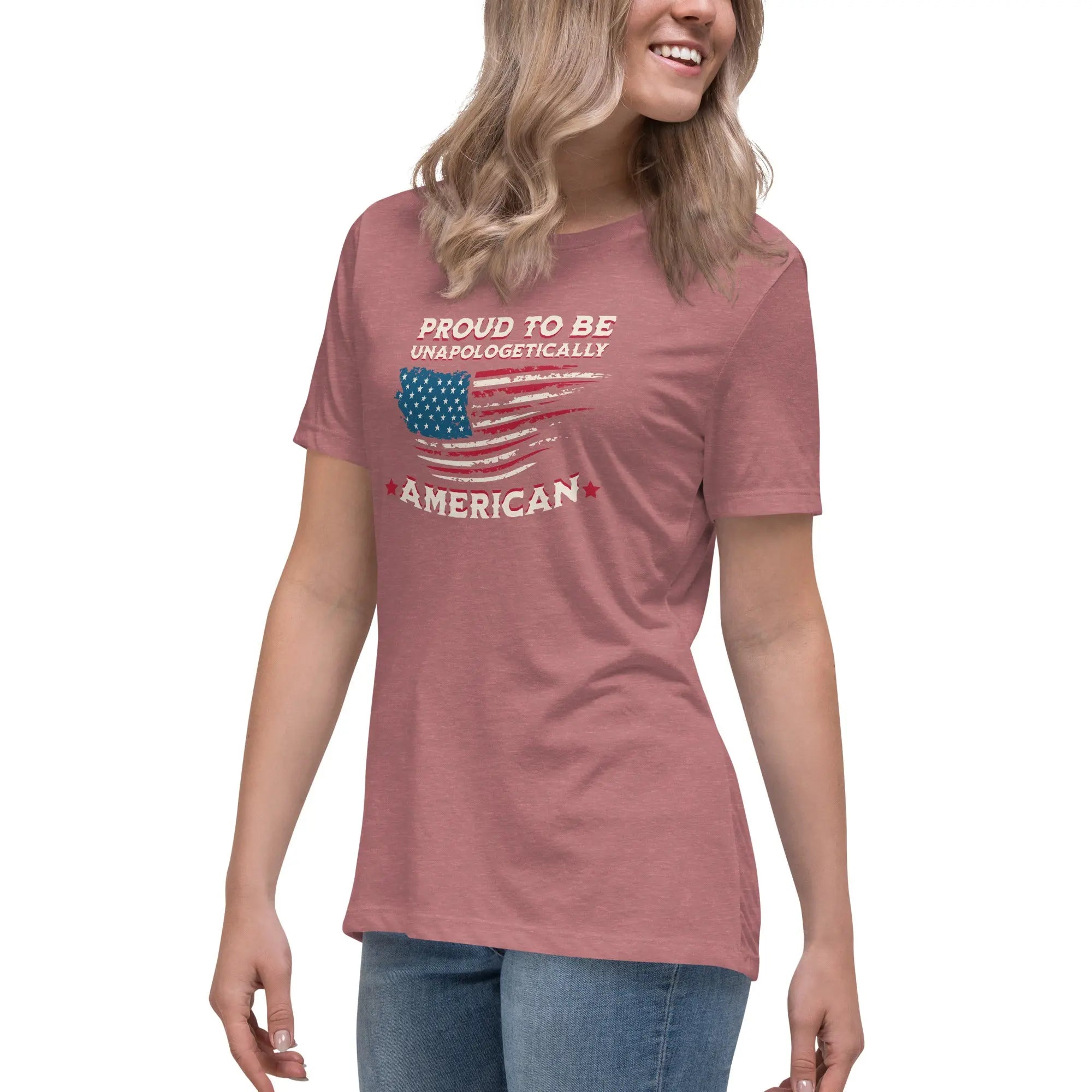 A woman wearing a heather mauve patriotic t-shirt with the American flag and "Proud To Be Unapologetically American" text.