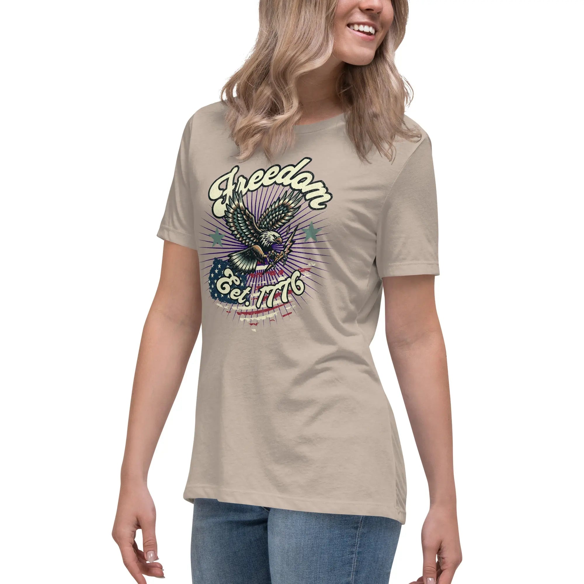 A woman wearing a heather stone patriotic t-shirt with an eagle and "Freedom Est. 1776" text.